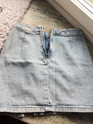 Ljusblå jeanskjol med slits - Snygg ljusblå jeanskjol i kort modell med dragkedja framtill och slits bak. Klassisk femficksdesign och raka linjer, perfekt till sneakers eller boots. Enkel att matcha med olika toppar för en cool look.