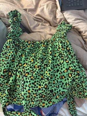 Grön leopardmönstrad linnetopp - Frakten står man själv för.Säljer en grön linnetopp med leopardmönster och breda, rynkade axelband. Toppen har en smockad struktur som ger en stretchig och bekväm passform. Perfekt för dig som vill sticka ut med färg och mönster!