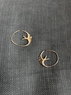 Guldiga örhängen med svalor - Unika örhängen i guldtonad metall med en elegant svala som motiv. De är tunna och runda med en stilren design som sticker ut. Perfekt för dig som gillar djurmotiv och vill ha något annorlunda. Säljs som ett par.