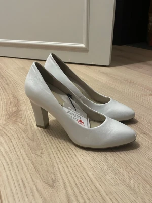 Vita pumps från Tamaris med klack - Snygga vita pumps från Tamaris med rund tå och stabil klack. Skorna är i läder och har en klassisk, stilren design. Perfekta för dig som gillar en elegant look och vill ha bekväma klackar med AntiShokk-teknologi.