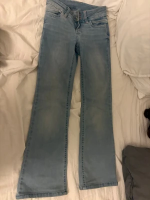 Ljusblå bootcut jeans från nelly  - Säljer ett par ljusblå bootcut jeans från nelly  med klassisk femficksdesign och snyggt broderad bakficka i orange. Jeansen har normal midja och är tillverkade i denim med lätt tvättad look. Perfekta för en avslappnad och trendig stil.