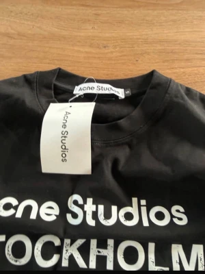 Svart långärmad topp Acne Studios - Svart långärmad topp från Acne Studios med vit text 'Acne Studios STOCKHOLM 1996' framtill. Klassisk rund halsringning och rak passform. Tillverkad i mjuk bomull, perfekt för en stilren och avslappnad look.