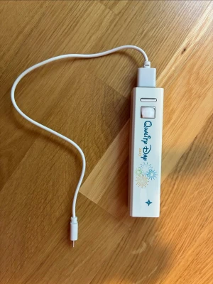 Powerbank vit - Vit powerbank med tryck. Rektangulär form med USB-port och medföljande vit laddningskabel. Dekorerad med färgglada fyrverkerimotiv och blå text. Perfekt för att ladda mobilen på språng. Endast använd några gånger, så den är i nyskick.