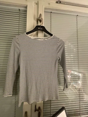 Randig topp från Holly & Whyte - Snygg långärmad topp från Holly & Whyte by Lindex i svartvitt randigt mönster. Toppen har rund halsringning och är tillverkad i ett ribbat material som ger en skön passform. Perfekt att styla med jeans eller kjol.