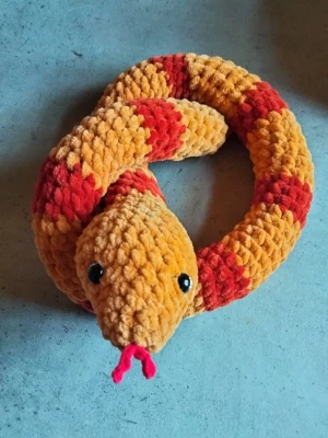 Virkat Gosedjur orm i orange och rött - Supermjuk och fluffig orm som gosedjur, virkad i orange och rött garn med svarta ögon och rosa tunga. Perfekt som mysig prydnad eller leksak. Gjord i tjockt, mjukt material som känns skönt att krama.