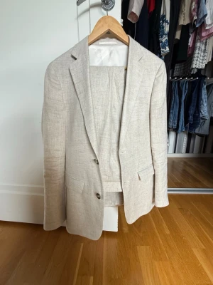 Beige linnékostym från Dressmann - Snygg beige kostym från Dressmann i 100% linne. Slim fit-modell med klassisk kavaj och matchande byxor. Perfekt för dig som vill ha en stilren och luftig look. Kavajen har två knappar och fickor framtill. storlek byxor 31-32 och storlek kavaj 44R. Passar perfekt inför vårens bal eller student. 