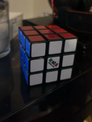 Rubiks kub 3x3 klassisk färg - En klassisk Rubiks kub 3x3 med färgerna röd, blå och vit synliga. Kuben har svart ram och färgade klistermärken på varje sida. Perfekt för dig som gillar kluriga pussel och vill utmana hjärnan.