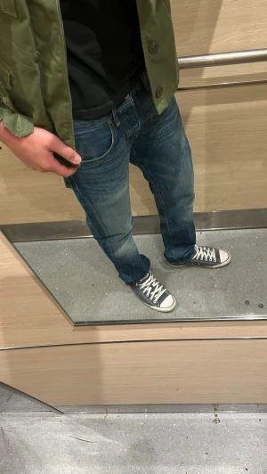 Blå raka jeans med klassisk passform - Säljer ett par blå jeans med rak passform och normal midja. Jeansen har fem fickor och klassiska kontrastsömmar. Materialet är denim i bomull och färgen är en tvättad blå nyans. Perfekta för en avslappnad och stilren look.