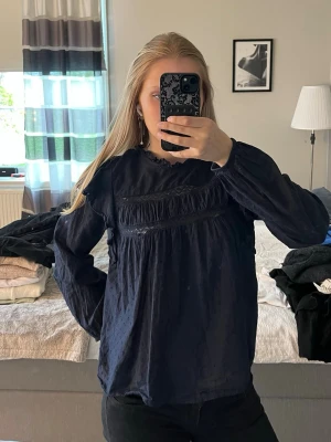 Mörkblå blus med spetsdetaljer - Mörkblå blus med långärmad design och fina spetsdetaljer över bröstet. 