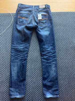 LIMITED EDITION -Nudie Jeans Fearless Freddie - Säljer ett par snygga blå jeans från Nudie Jeans, modell Fearless Freddie. Jeansen har klassisk femficksdesign, orangea sömmar och är gjorda i 100% ekologisk bomull. De har en schysst tvätt med slitningar och raka ben.