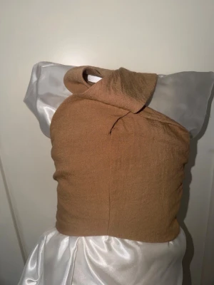 Beige omlottopp med knyt - Trendig beige omlottopp med snygg knytning i ryggen och hög hals. Toppen är ärmlös och har en stilren, figurnära passform. Perfekt för dig som vill ha en unik och modern look. Materialet känns mjukt och bekvämt mot huden.