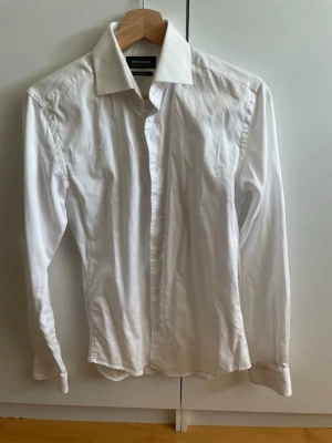 Vit extra slim fit skjorta Dressmann - Klassisk vit skjorta från Dressmann i extra slim fit-modell. Tillverkad i stretchig bomull för en skön och smidig känsla. Skjortan har långa ärmar, knappar framtill och en stilren krage. Perfekt för dig som gillar en tajtare passform.