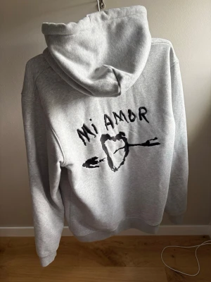 Grå hoodie med Mi Amor-tryck - Säljer en grå hoodie, är i storlek M det vill inga tecken på användning, den ser helt ny ut. Ny pris 844kr