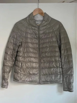 Ljusgrå dunjacka med dragkedja från Uniqlo! - Snygg ljusgrå dunjacka med quiltat mönster och hög krage. Jackan har en stilren design med raka linjer och dragkedja framtill. Perfekt för kalla dagar när du vill hålla värmen och ändå se fräsch ut. Storlek L, men passar en S i västerländsk storlek. 