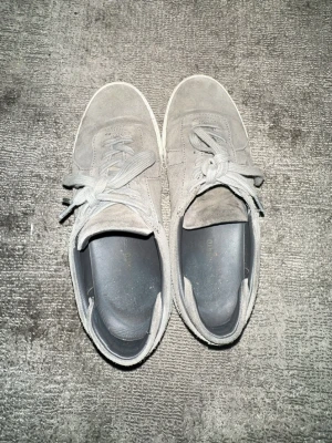 Gråa sneakers i mocka - Snygga grå sneakers i mocka med vita sulor och klassisk snörning. Skorna har en stilren och enkel design som passar till det mesta. Perfekta för dig som gillar en clean och avslappnad look.