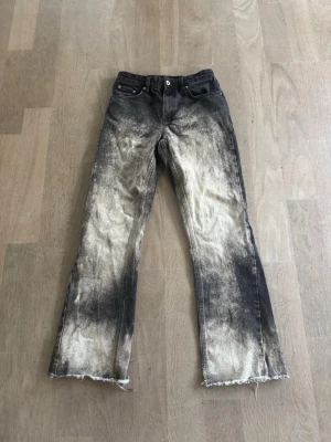 Svarta custom flared jeans med blekt och sliten look - Unika svarta jeans med kraftig blekt effekt och slitna, fransiga benslut. Raka ben och klassisk femficksmodell. Jeansen har en cool, vintageinspirerad streetstil och är tillverkade i bomull. Perfekta för dig som gillar en edgy och personlig stil.