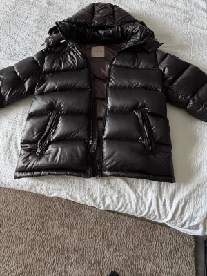 Svart Moncler dunjacka med huva - Säljer en svart Moncler dunjacka med huva och dragkedja. Jackan har klassisk quiltad design, Moncler-logga på ärmen och på insidan av jackan, båda med nfc kapabilitet. Flera fickor med dragkedja och snygga detaljer. Perfekt för kalla dagar och riktigt stilren look. Det är storlek S. Bättre köpa tidigt än för sent!