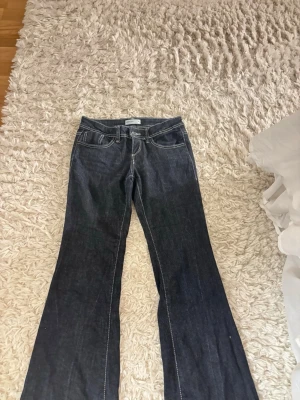 Mörkblå bootcut jeans - Säljer ett par mörkblå bootcut jeans med vita kontrastsömmar och klassisk femficksdesign. Jeansen har låg midja och utsvängda ben, perfekta! Materialet är denim i bomull. Storleken är 34 men dom är väldigt stretchiga i midjan och benen! Jag är 164 och dom är perfekta i längden!