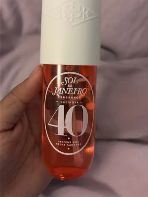 Sol de Janeiro Cheirosa 40 Parfymmist - En snygg parfymmist från Sol de Janeiro i doften Cheirosa 40. Flaskan är genomskinlig med en rosa-orange vätska och har ett vitt lock med präglad logga. Perfekt att spraya på för en fräsch och tropisk känsla.