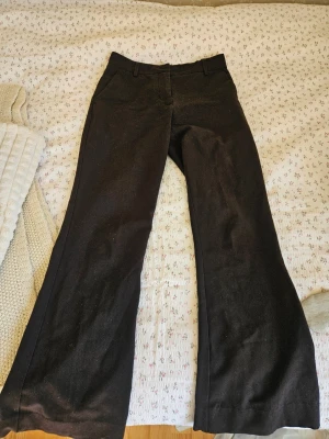 Svarta utsvängda kostymbyxor - Säljer ett par svarta kostymbyxor med utsvängda ben och mellanhög midja från MSCH Copenhagen. Lite urtvättade i färgen och själva "handtaget" på dragkedjan har en defekt (se bild 3), utöver det är de i fint skick! 🥰 stl xs men passar bra på mig som bär S