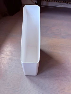 Vit tidningsställ i plast - Säljer ett stilrent vitt tidningsställ i plast med rektangulär form och snedskuren öppning. Perfekt för att organisera papper, tidningar eller mappar på skrivbordet eller i bokhyllan.