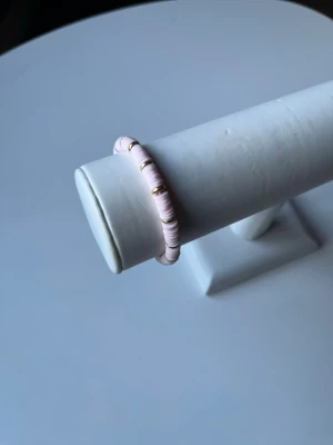  Rosa armband med lite gulddetaljer  -  Ett somrigt rosa armband med lite gulddetaljer som har elastiskt band så att det är lätt att ta av och på. Armbandet är även handgjort.