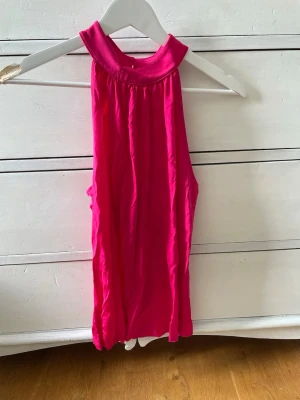 Rosa topp - Säljer en ärmlös topp i stark rosa med hög halsringning. Toppen har en lös passform. Obs skrynklig på bilden, går att få slät. Sitter som en S i storleken