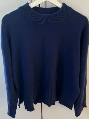 Mörkblå stickad tröja - Mysig mörkblå stickad tröja med ribbad hals och slitsar i sidorna. 