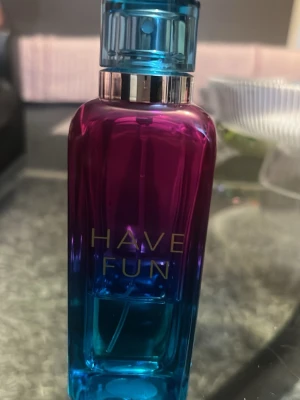 I använt skick finns lite i… Have Fun parfymflaska i blå och lila - Snygg parfymflaska med texten 'HAVE FUN' i guld. Flaskan har en cool färgskiftning från lila upptill till blå nedtill och ett matchande blått spraylock. Modern, rektangulär form som känns trendig och ungdomlig. Perfekt för dig som gillar färgstarka accessoarer.