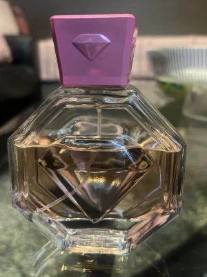 Parfymflaska med diamantmotiv - Snygg parfymflaska i transparent glas med ett diamantformat mönster på framsidan och ljust rosa lock. Flaskan har en modern, geometrisk form och känns lyxig och trendig. Perfekt för dig som gillar unika och stilrena doftflaskor.