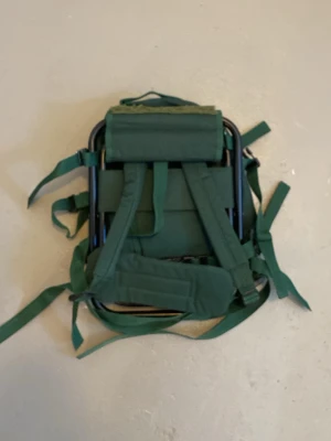 Grön ryggsäck med inbyggd stol - Säljer en grön ryggsäck med inbyggd fällbar stol och vadderad sits. Ryggsäcken har flera justerbara remmar och vadderade axelband för extra komfort. Perfekt för dig som vill ha både packning och sittplats i ett. Materialet är slitstark textil och metallram.