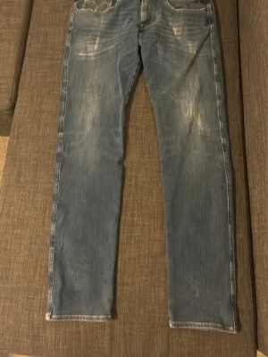 Ljusblå raka jeans med slitningar / Replay - Säljer ett par ljusblå jeans med raka ben och snygga slitningar framtill. Jeansen har klassisk femficksdesign och kontrastsömmar. Perfekta för en avslappnad och trendig look. Materialet är denim i bomull.