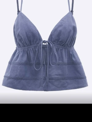 Blå crop top med tunna axelband - Snygg blå crop top med tunna justerbara axelband och knytning framtill. Toppen har en lätt rynkad design och dekorativa sömmar som ger en bohemisk känsla. Tillverkad i ett tunt, luftigt tyg som passar perfekt till sommaren.
