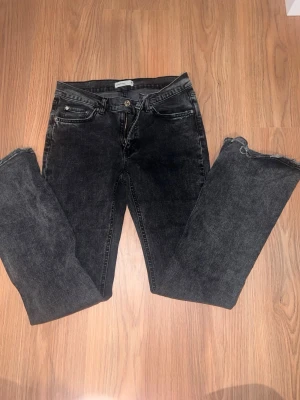 Svarta raka jeans med rå kant - Säljer ett par svarta jeans med rak passform och rå, fransig kant nedtill. Jeansen har klassisk femficksdesign och knappgylf. Perfekta för en avslappnad och trendig look.