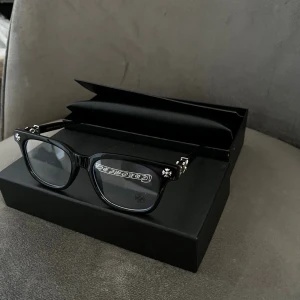 Chrome Hearts Cox Ucker - Snygga svarta solglasögon från Chrome Hearts med rektangulär form och silverfärgade detaljer vid gångjärnen. Glasögonen har en klassisk och stilren look med tydlig logga på sidan. Perfekta för dig som vill ha en exklusiv accessoar. Priset är ej hugget i sten så skäms inte vid förslag 