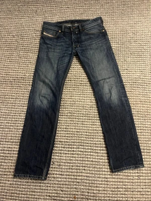 Mörkblå jeans från Diesel - Säljer ett par klassiska mörkblå jeans från Diesel Jeans med raka/ bootcut ben och fem fickor. Jeansen kontrastsömmar samt en patch med logga bak i midjan. Perfekta till din vardagsstil!