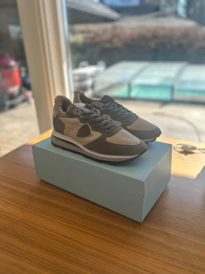 OANVÄNDA Philippe Model Herrskor 43 Beige  - Snygga sneakers från Philippe Model i beige och brun mocka med vita detaljer och yttersula, perfekta inför våren. Skorna har aldrig haft en fot i sig, aldrig klivit ett steg, sprillans nya som ni kan se på den andra bilden. De är självklart äkta och kvitto ingår. Antingen kan ni hämta dem i sollentuna eller så kan jag frakta de med köparskydd. Storleken är 43, är något större i passform. nypris ligger på 3500kr, mitt pris endast 1399kr. 