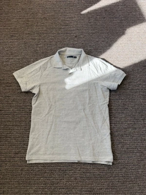 Ljusgrå pikétröja från 157 - Klassisk ljusgrå pikétröja från 157 med korta ärmar och krage. Tröjan har en enkel och stilren design utan synliga loggor eller mönster, perfekt till både jeans och shorts. Tillverkad i mjuk bomull för skön känsla hela dagen.