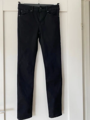 Svarta skinny jeans med hög midja, storlek 160 - Säljer ett par svarta skinny jeans med hög midja och klassisk femficksdesign i mycket fint skick. Jeansen har smal passform och är tillverkade i stretchigt denimtyg för extra komfort. Närbildena gör att de ser gråa ut, men jeansen är helsvarta. På insidan av midjan finns också en resår för att kunna få till helt rätt passform.  Perfekta till en avslappnad eller trendig look.