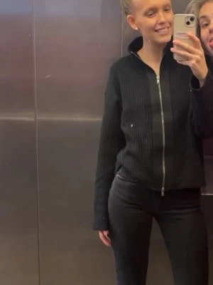 Svart ribbad ziptröja - Säljer en svart ribbad ziptröja med hög krage och långa ärmar. Tröjan har en hel dragkedja framtill och är i ett mjukt stickat material som ger en clean och stilren look.