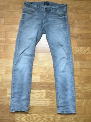 Ljusgrå slim fit jeans från Jack & Jones - Snygga ljusblå slim fit jeans från Jack & Jones med klassisk femficksdesign och diskreta sömmar på bakfickorna. Jeansen har normal midja och är tillverkade i mjuk denim med lite stretch för extra komfort.