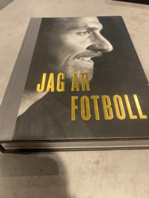 Jag är Fotboll - Fotobok - En snygg och inspirerande bok med titeln 'Jag är Fotboll'. Omslaget är svart med guldfärgad text och har en hård pärm med grå rygg. Boken innehåller många färgbilder från fotbollsmatcher och spelare, perfekt för dig som älskar fotboll och vill ha en bok fylld med action och känsla.