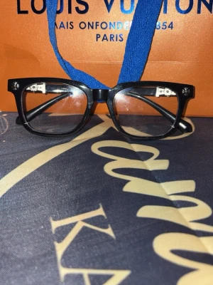 Svarta chrome heart glasögon  - Snygga svarta chrome heart solglasögon med klassisk rektangulär form. Bågarna har silverfärgade detaljer vid gångjärnen och logotyp på sidan. Perfekt accessoar för dig som vill ha en lyxig och trendig look.