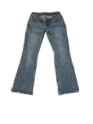 Vintage lowwaist bootcut jeans med slitningar  - Säljer ett par blå bootcut jeans med lätt slitna detaljer och klassisk femficksmodell. Jeansen har låg midja och är tillverkade i denim med en snygg tvättad look. Perfekta för dig som gillar retrostil och vill ha ett par jeans med lite vidare ben.