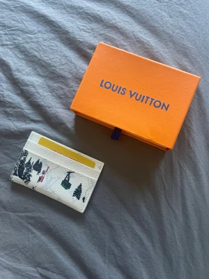  vit korthållare - Säljer en snygg vit korthållare med coolt vinterlandskapsmotiv, inklusive träd och skidliftar. Tillverkad i tåligt canvasmaterial och har flera fack för kort. Perfekt för dig som vill ha något unikt och stilrent i fickan.