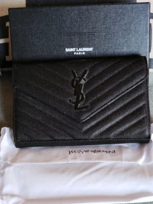 Svart Wallet on a chain - Snygg svart kuvertväska med ikoniska loggan framtill. Väskan har ett quiltat mönster och är gjord i ett caviarläder.. Perfekt storlek för det viktigaste och har en stilren, modern look med avtagbar kedja. Kommer med dustbag och box