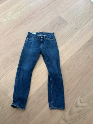Mörkblå raka jeans - Säljer ett par klassiska mörkblå jeans med rak passform och fem fickor. Jeansen har en tidlös look med kontrastsömmar och knappgylf. Perfekta för dig som gillar en enkel och clean stil.