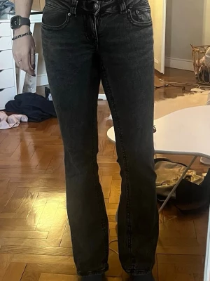 Svarta bootcut jeans med tvättad look - Säljer ett par svarta bootcut jeans med tvättad finish och klassiska fem fickor. Jeansen har låg midja. 