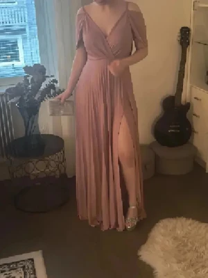 Balklänning❤️ - Elegant långklänning i mjukt, flytande tyg i en dämpad rosa ton. Klänningen har offshoulder-ärmar, omlott över bysten och en hög slits framtill. Perfekt för bal eller festligare tillfällen. Supersnygg och formar kroppen såååå fint❤️Slutsåld