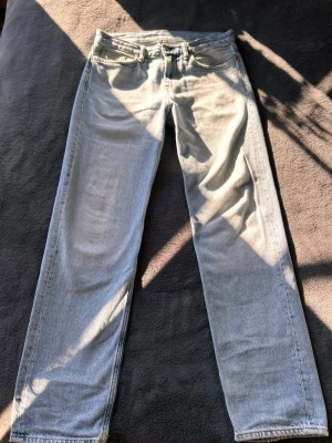 Ljusblå raka jeans - Säljer ett par ljusblå jeans med rak passform och klassisk femficksdesign. Jeansen har normal midja och är tillverkade i denim med en snygg tvättad look. Perfekta för en avslappnad och trendig stil.